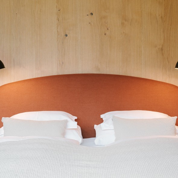 Doppelbett mit rostrotem Kopfteil vor einer Holzwand